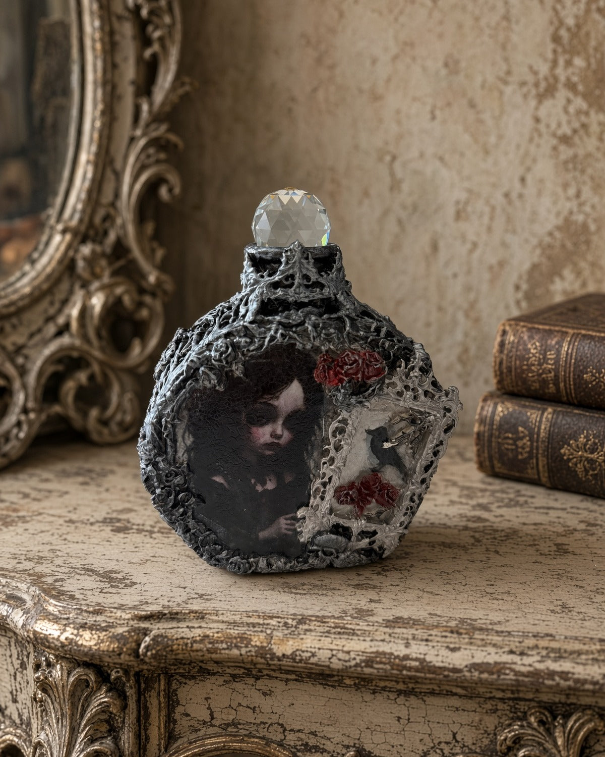 Front of gothic decoupage glass bottle with its included crystal-ball stopper and silver-black textured relief on a cream table