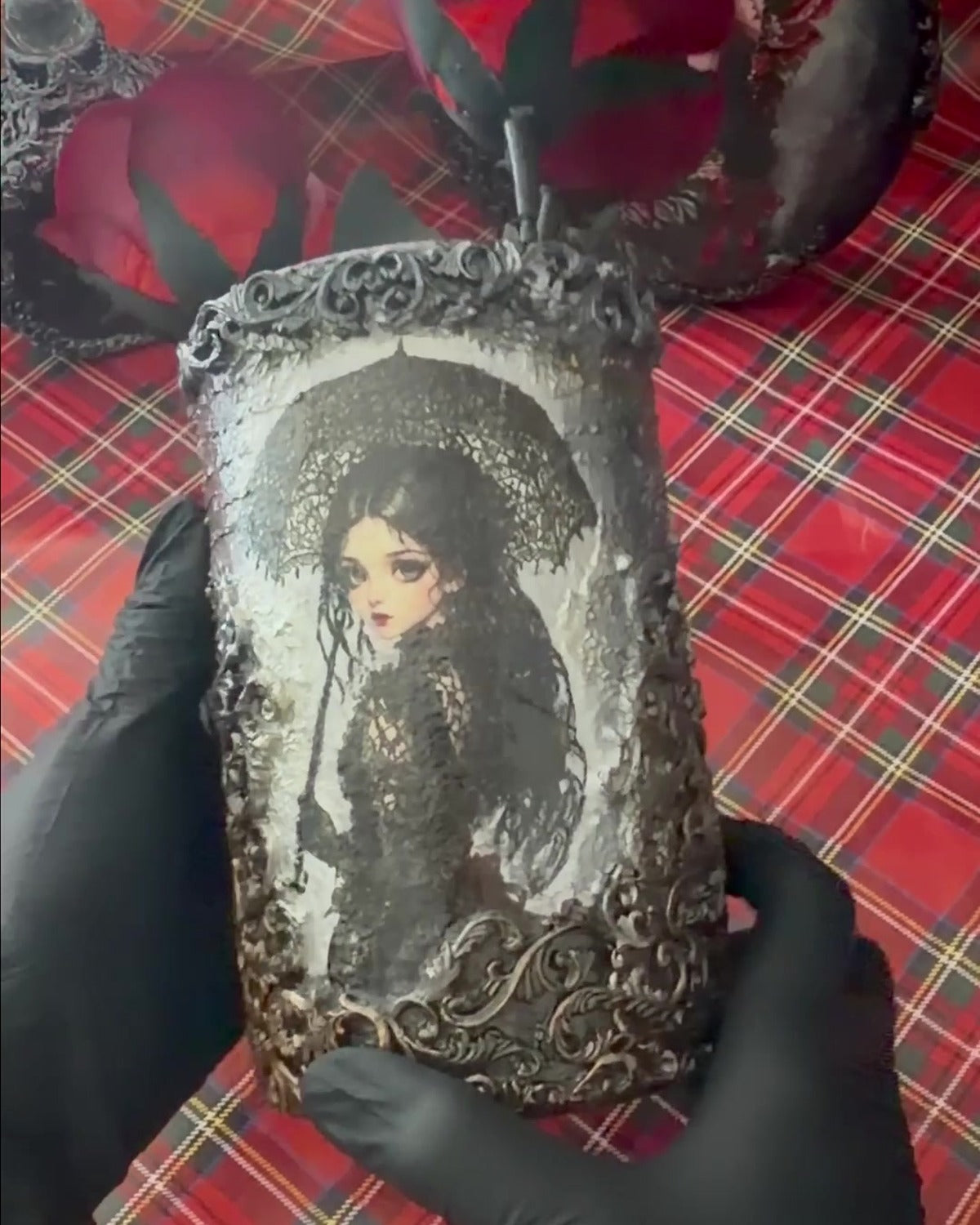 Gothic portraits decoupage glass vase held in black-gloved hands to show its size, red roses behind